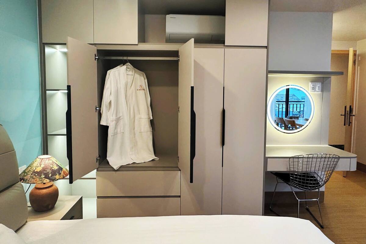 Una habitación de hotel moderna con vestidor, cama, escritorio con silla y ventanal circular.