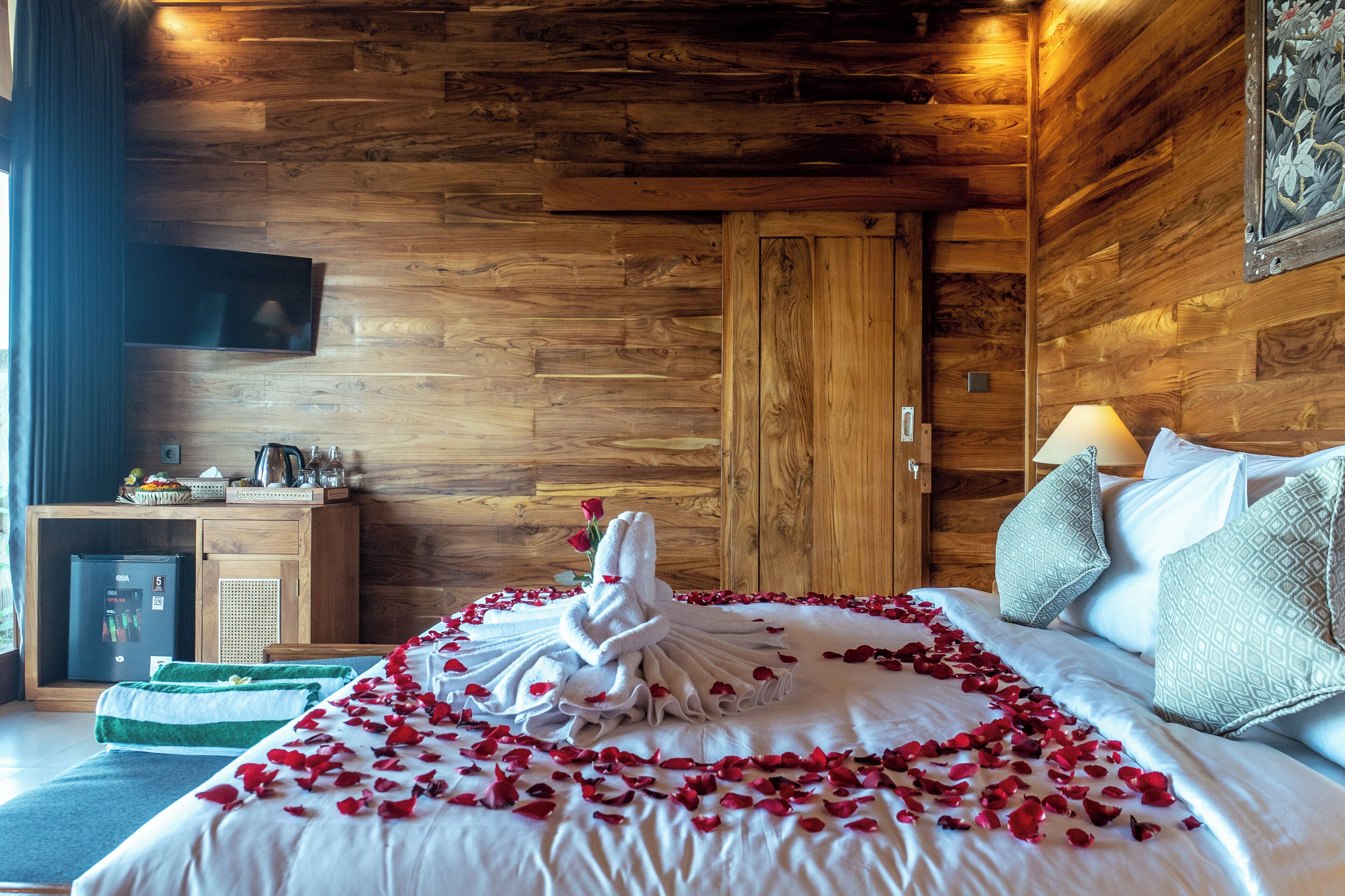 A wooden-paneled room with a bed, pillows, a television, and a small desk with a kettle.