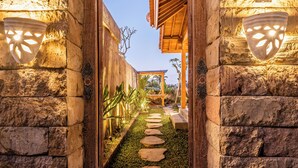 Un sendero de piedra que conduce a una construcción de madera con pérgola, rodeada de muros de piedra y luminarias decorativas.