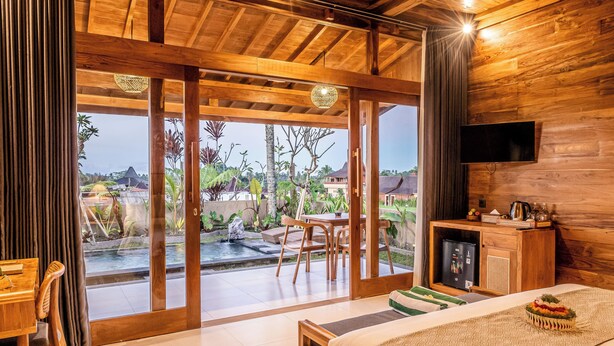 Interior de madera con una cama, un televisor y vistas a un jardín y piscina.