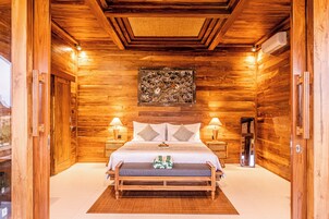 A wooden-paneled bedroom with a large bed, two bedside tables, a mirror, and a ceiling artwork.