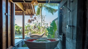 Un baño moderno con una bañera grande, una ducha y vistas a un jardín tropical.