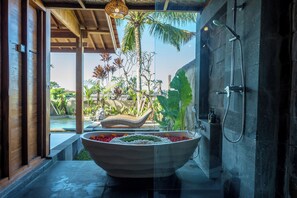 Un baño moderno con una bañera grande, una ducha y vistas a un jardín tropical.