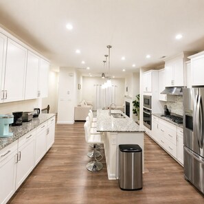 A modern kitchen with white cabinets, stainless steel appliances, a granite countertop, and a central island with bar stools. - Lux 4BR,3.5Bath townhome, perfect for groups (Cary)