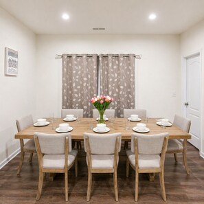 Uma sala de jantar com uma mesa de madeira posta para seis pessoas, seis cadeiras e um vaso de flores.