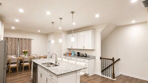 A modern kitchen with white cabinetry, a granite countertop island, and a dining area with a table and chairs. - Lux 4BR,3.5Bath townhome, perfect for groups (Cary)