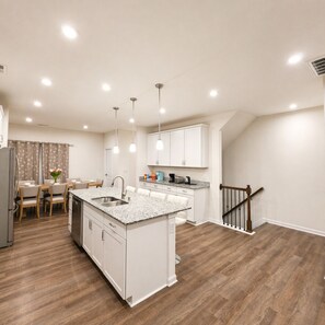 A modern kitchen with white cabinetry, a granite countertop island, and a dining area with a table and chairs. - Lux 4BR,3.5Bath townhome, perfect for groups (Cary)