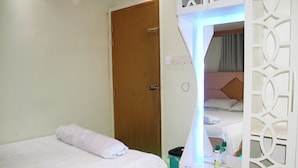 Quarto de hotel com uma cama, porta de madeira, espelho e uma mesinha com artigos de higiene pessoal.
