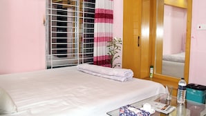 Quarto de hotel com cama, mesa de vidro com artigos de higiene pessoal, espelho e janela com persianas.
