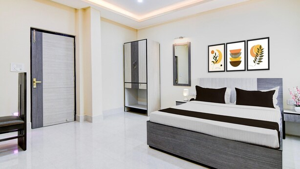 A modern bedroom with a large bed, a wardrobe, a bench, and a door. - Premium Collection O Joka Industrial Plaza (Alipur)