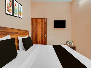Ein Hotelzimmer mit Holz-Kopfteil, einem Bett mit weißer und schwarzer Bettwäsche, einem an der Wand montierten Flachbildfernseher und einem kleinen Tisch mit Toilettenartikeln.