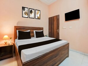Een verzorgde slaapkamer met een houten bedframe, een nachtkastje met een lamp, en een flatscreen televisie aan de muur.