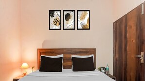Una cama con cabecera de madera, dos almohadas negras, una colcha blanca y una mesita de noche con una lámpara y una botella.