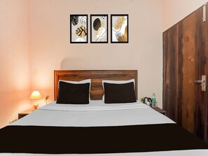 Ein Bett mit Holz Kopfteil, zwei schwarze Kissen, eine weiße Tagesdecke und ein Nachttisch mit Lampe und einer Flasche.