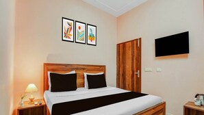 Un dormitorio con una cama de madera, una mesita de noche con una lámpara, un televisor montado en la pared y tres cuadros enmarcados sobre la cama.