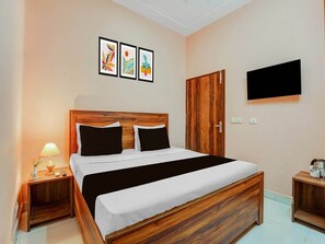 Ein Schlafzimmer mit einem hölzernen Bett, einem Nachttisch mit Lampe, einem an der Wand montierten Fernseher und drei gerahmten Kunstwerken über dem Bett.