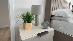 Une table de chevet avec une lampe, une horloge et une plante en pot.