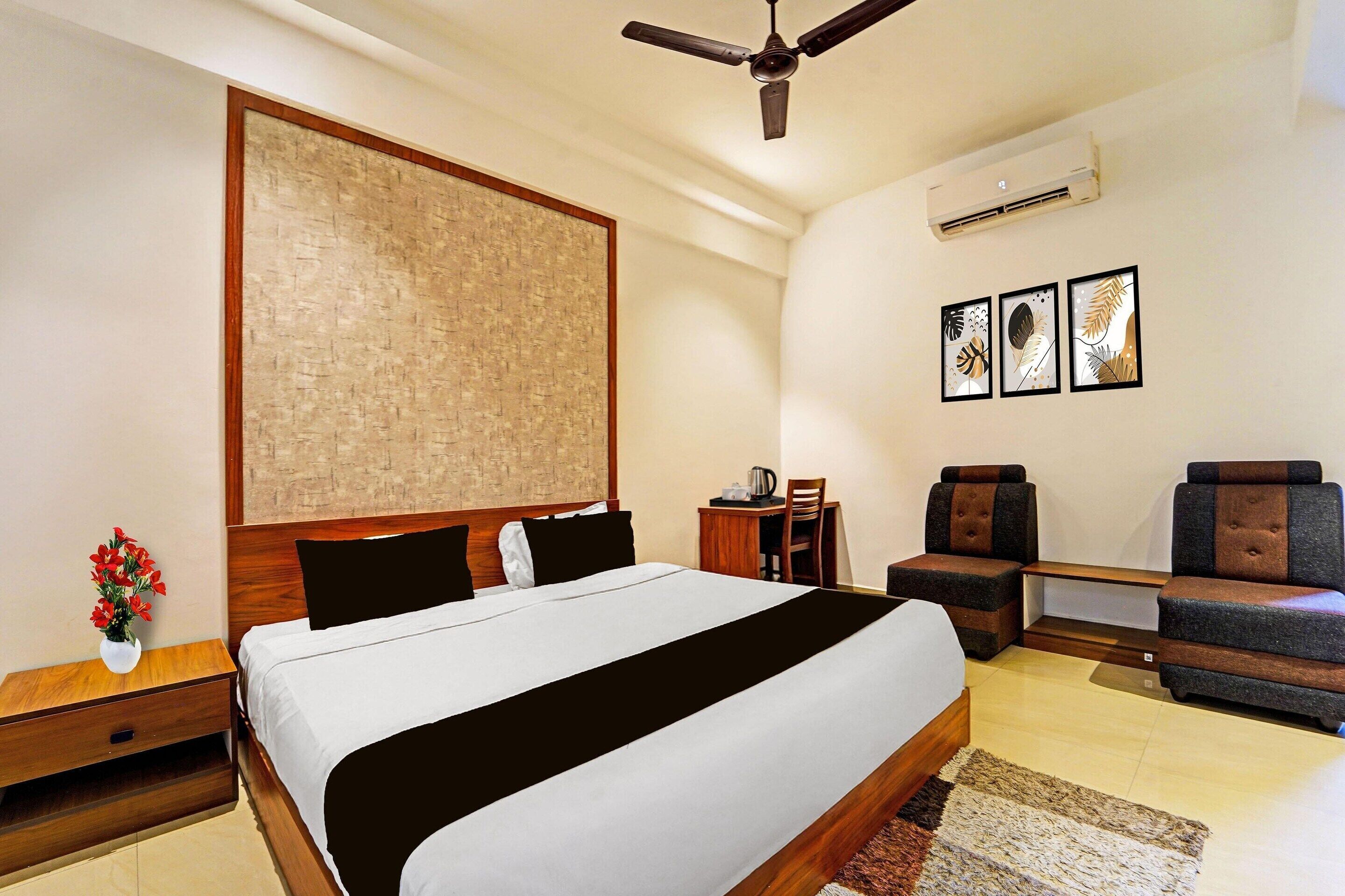 A hotel room with a large bed, a desk, a chair, a ceiling fan, and three framed pictures on the wall.