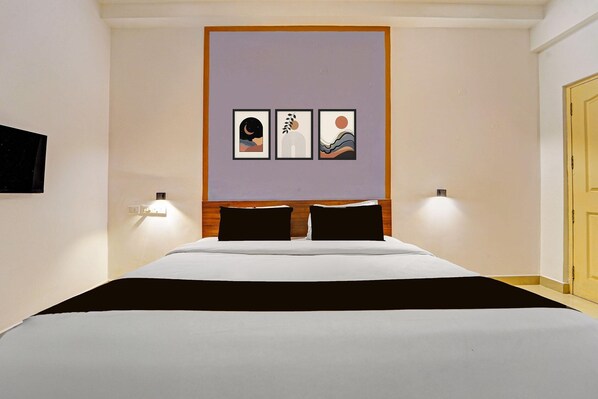 A hotel room with a bed, a headboard, a wall-mounted TV, and three framed artworks.