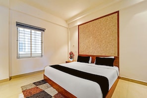 A hotel room with a bed, a window with blinds, a nightstand with a vase of flowers, and a large abstract painting on the wall. - Classic The Beige Hotel (Kozhenchery)