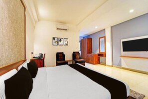 A hotel room with a large bed, a desk with a chair, a television, and a wardrobe. - Classic The Beige Hotel (Kozhenchery)