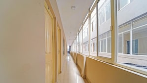 A long, narrow hallway with doors on one side and windows on the other, leading to a building with a white exterior. - Classic The Beige Hotel (Kozhenchery)