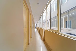A long, narrow hallway with doors on one side and windows on the other, leading to a building with a white exterior. - Classic The Beige Hotel (Kozhenchery)