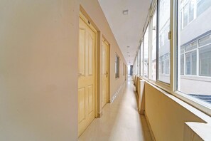 A long, narrow hallway with doors on one side and windows on the other, leading to a building. - Classic The Beige Hotel (Kozhenchery)