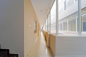 Un pasillo largo y estrecho con suelo de baldosas, ventanas amplias a un lado y una escalera al otro.