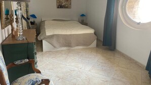 Quarto com cama, cadeira, cômoda, abajur, quadro e janela.