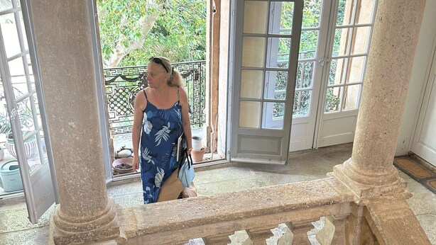 Mulher em frente a um vidro, com vista para o verde lá fora.