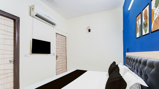 A hotel room with a bed, air conditioning unit, wall-mounted TV, and a blue accent wall. - Saver Doubleroyal Inn (New Delhi)