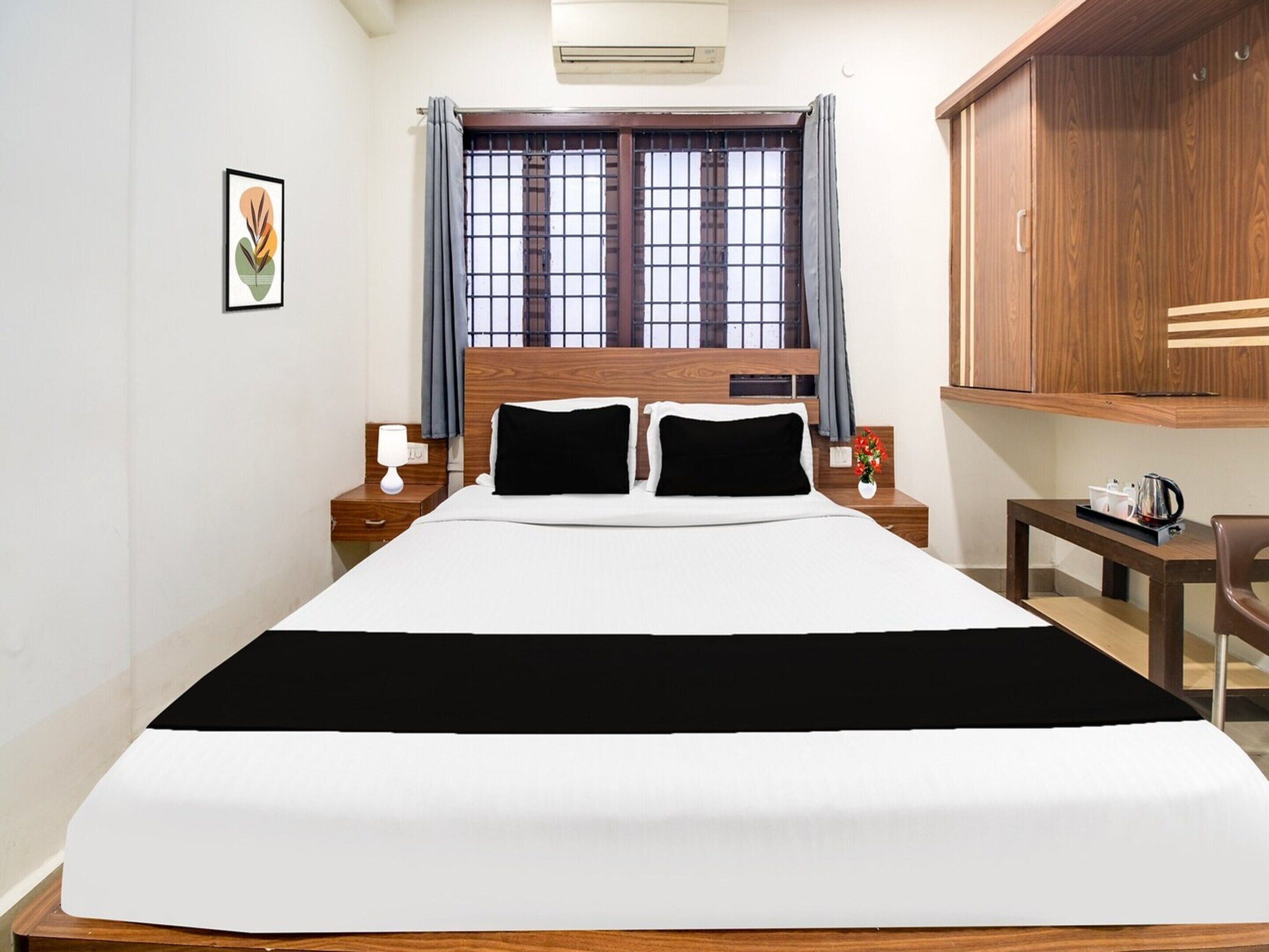A hotel room with a large bed, two bedside tables, a nightstand, a wooden wardrobe, a window with curtains, and a framed picture on the wall.