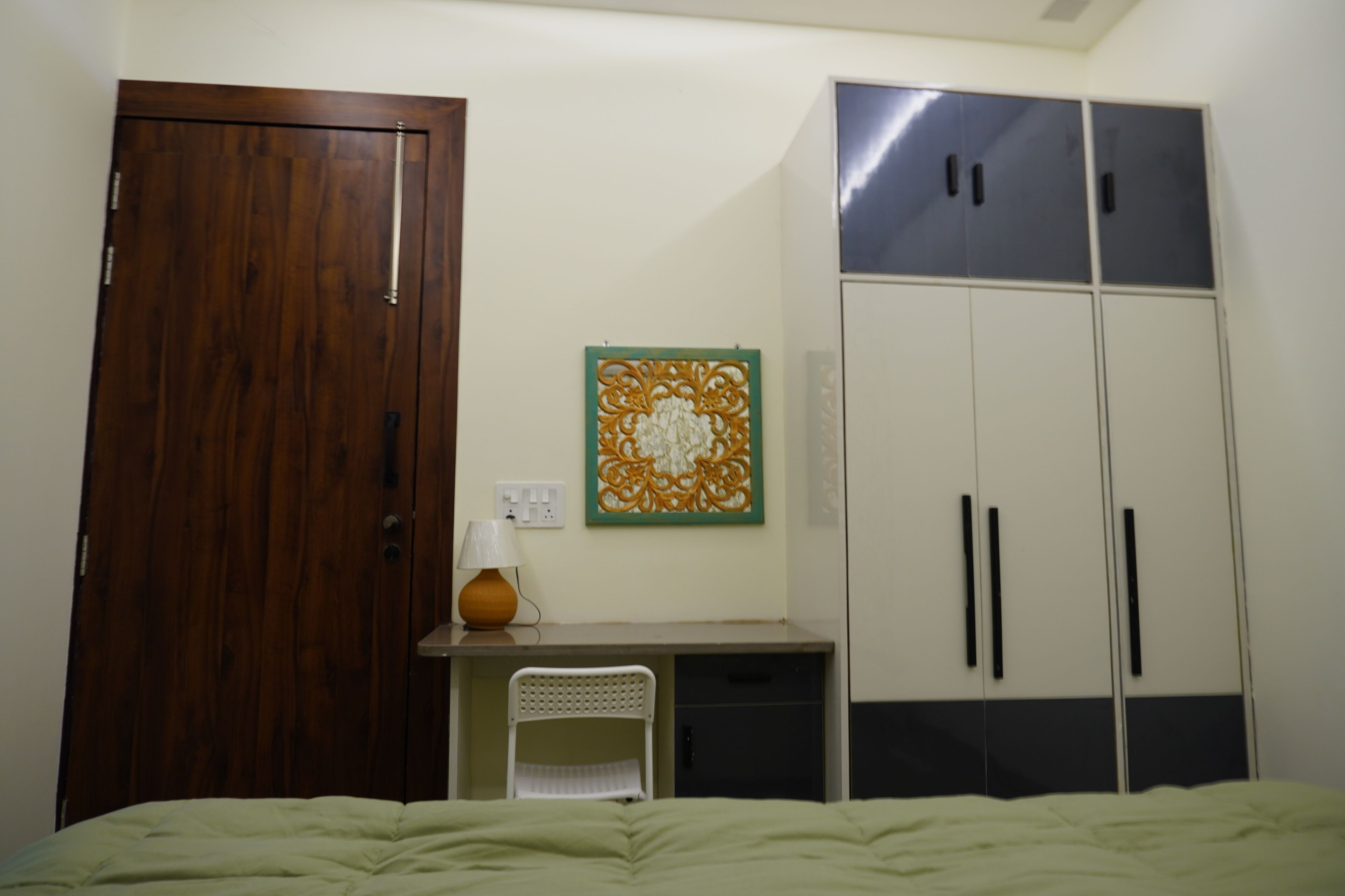 A bedroom with a bed, a desk, a chair, a wardrobe, and a wall decoration.