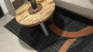 Un soggiorno moderno con un divano grigio, un tavolino rotondo in legno e tre opere d'arte incorniciate appese al muro.
