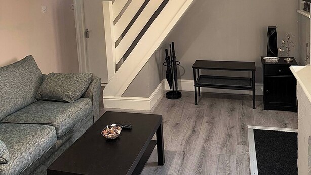 Ett vardagsrum med en soffa, ett soffbord, en lampa, en trappa och ett litet bord med en vas.
