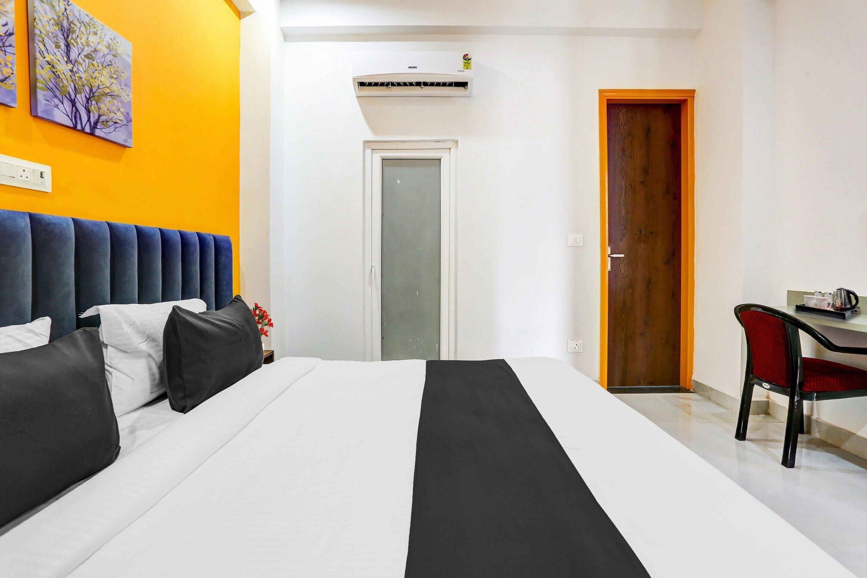 A hotel room with a bed, a desk, a chair, an air conditioning unit, and a door.