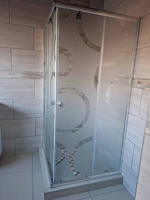 Une douche fermée par des parois de verre, au design moderne, avec des murs carrelés et un logo de marque bien visible.