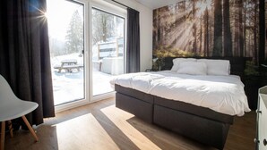 A bedroom with a bed, a chair, a large window, and a forest-themed wall. - Ferienwohnungen mit Skilift Direkt am Haus (Winterberg)