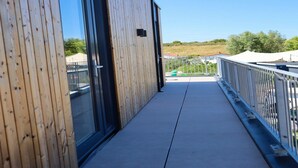 A modern building with a wooden exterior, a glass door, and a balcony with a metal railing. - 4-bedroom Stylish Bungalow by the Sea ('s-Gravenzande)