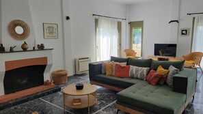 Ein Wohnzimmer mit Sofa, Fernseher, Kamin und Blick ins Freie.