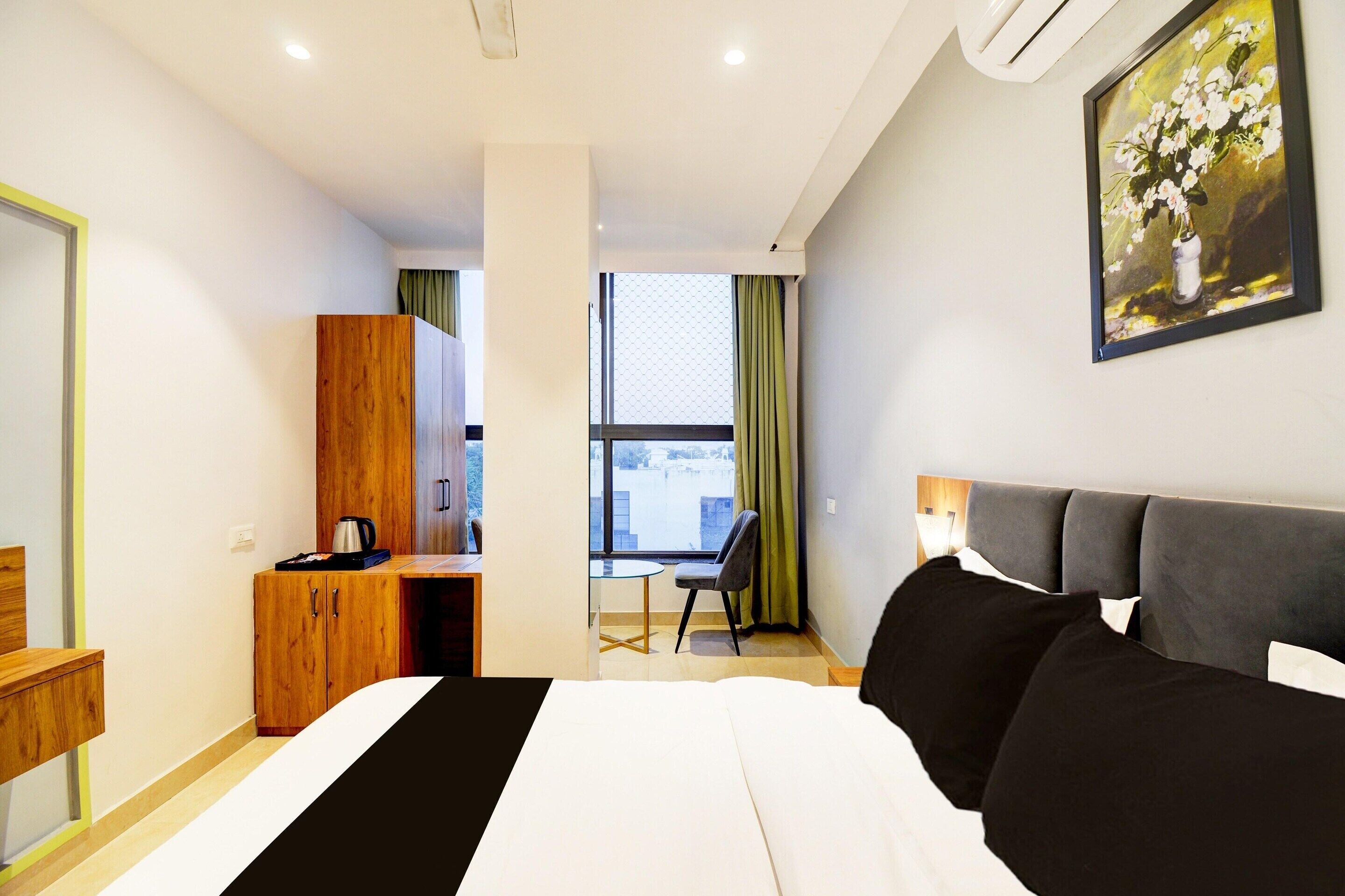A hotel room with a bed, a desk, a chair, a wardrobe, and a painting on the wall.