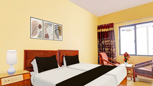A hotel room with a double bed, a bedside table with a lamp, a chair, a small table with a vase, and a window with curtains. - Hotel O Gajuwaka Near Kurmanpalem (Visakhapatnam)