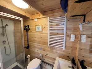 Une salle de bain aux murs lambrissés, équipée d’une douche, de toilettes, d’un lavabo et d’un porte-serviettes.