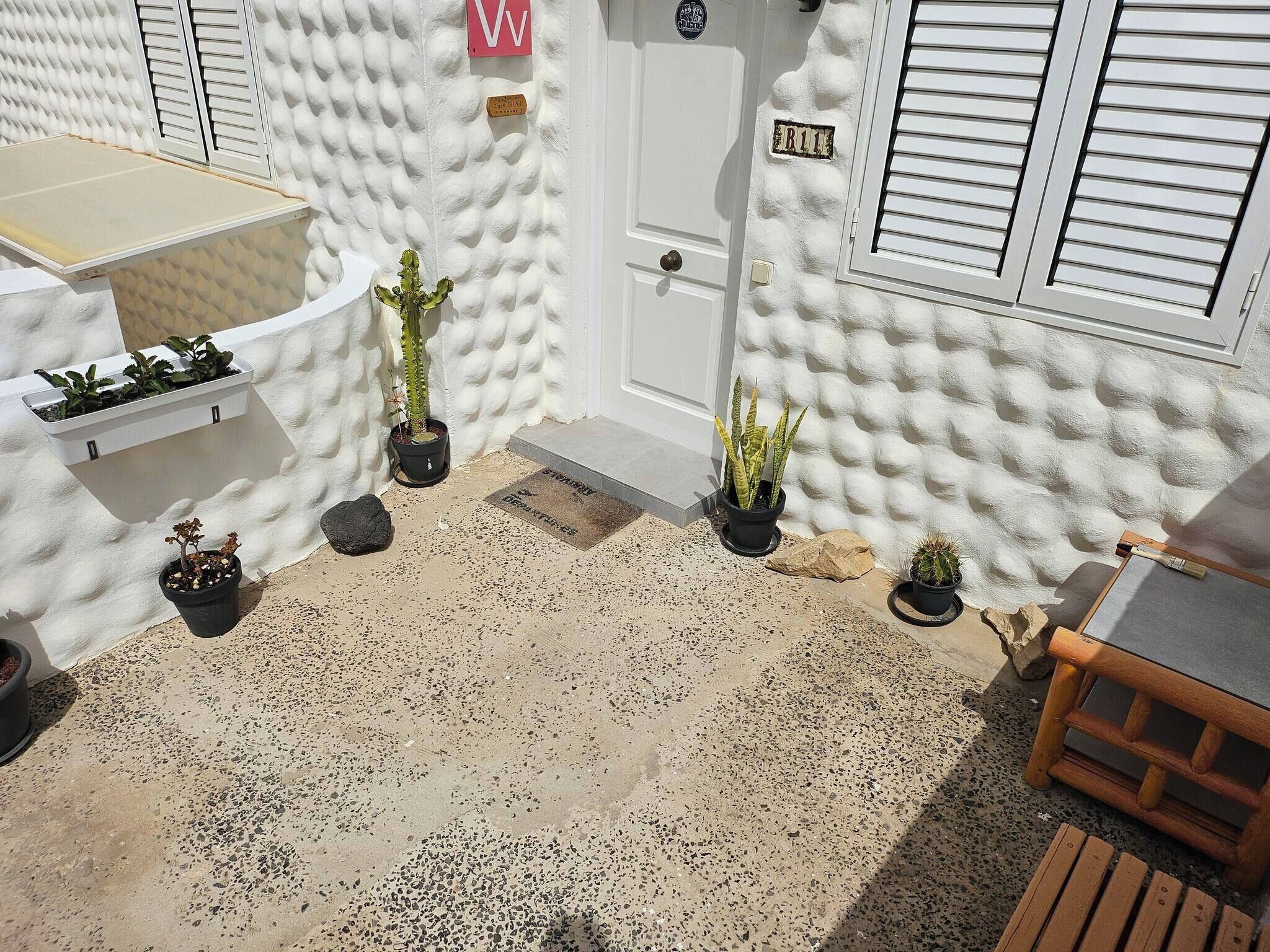 A white exterior wall with textured stucco, a white door with a mailbox, and potted plants.