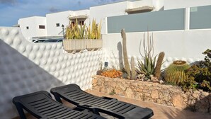 A modern outdoor patio with black lounge chairs, a white wall with a textured pattern, and a variety of desert plants. - Casa Del Sol Rio in Costa Calma (Costa Calma)