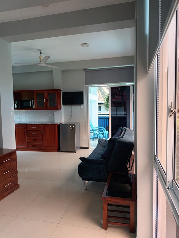 A living area with a sofa, a wooden table, a kitchen with cabinets and appliances, and a sliding glass door leading to an outdoor area.