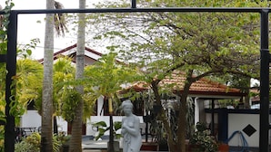 Ein Garten mit einer Statue, einem Rasen und einem Gebäude im Hintergrund.