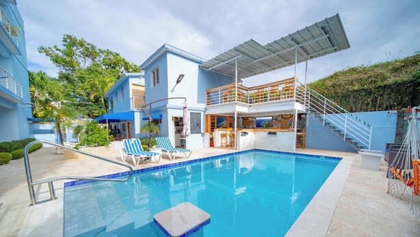Une piscine dotée d’un parasol, de chaises longues et d’un escalier menant à une terrasse supérieure.