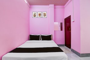 A room with pink walls, a bed with white and black bedding, and three framed pictures on the wall. - Super Deluxe Roomjalsaghar (Alipur)